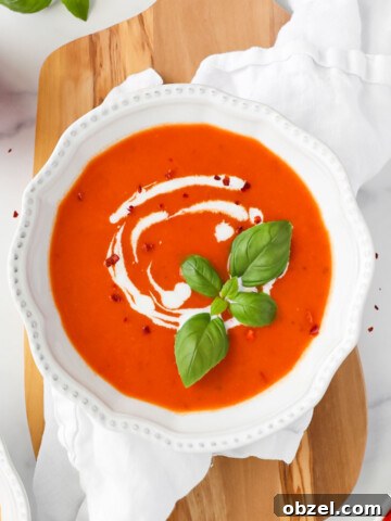 A white bowl filled with roasted red pepper soup garnished with basil.