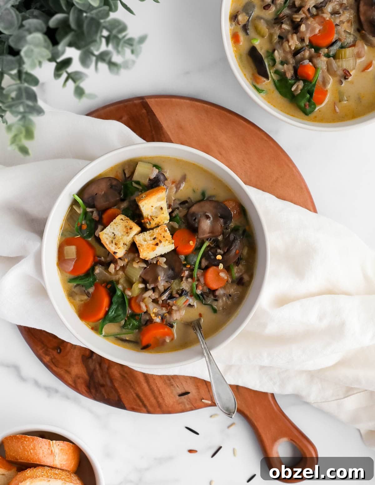 Creamy Wild Rice and Mushroom Soup Recipe 4 A large white bowl filled with rice and vegetable soup with a spoon.
