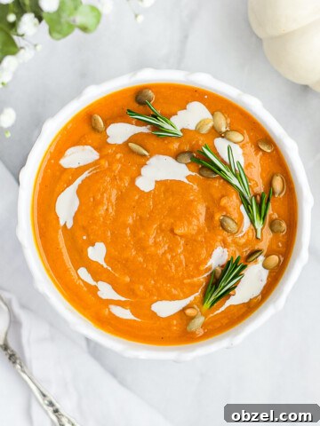 A white bowl with orange soup garnished with vegan crema and herbs.