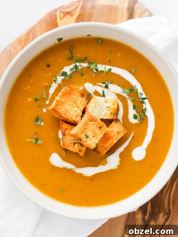 A white bowl with butternut squash apple soup topped with coconut milk drizzle and croutons.
