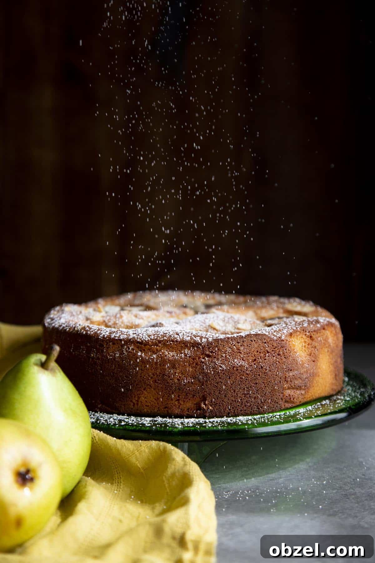 Pear Almond Cake topped with powdered sugar A pear almond cake on a green cake plate with powdered sugar raining down on it