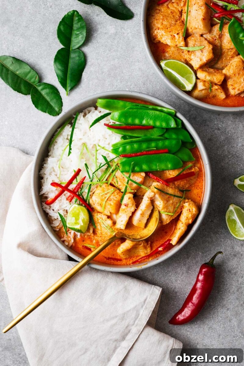5 Ingredient Thai Green Curry Recipe 15 A bowl with steamed jasmine rice, Thai fish red curry and snow peas topped with sliced red chile and kaffir lime leaves wit a golden serving spoon.