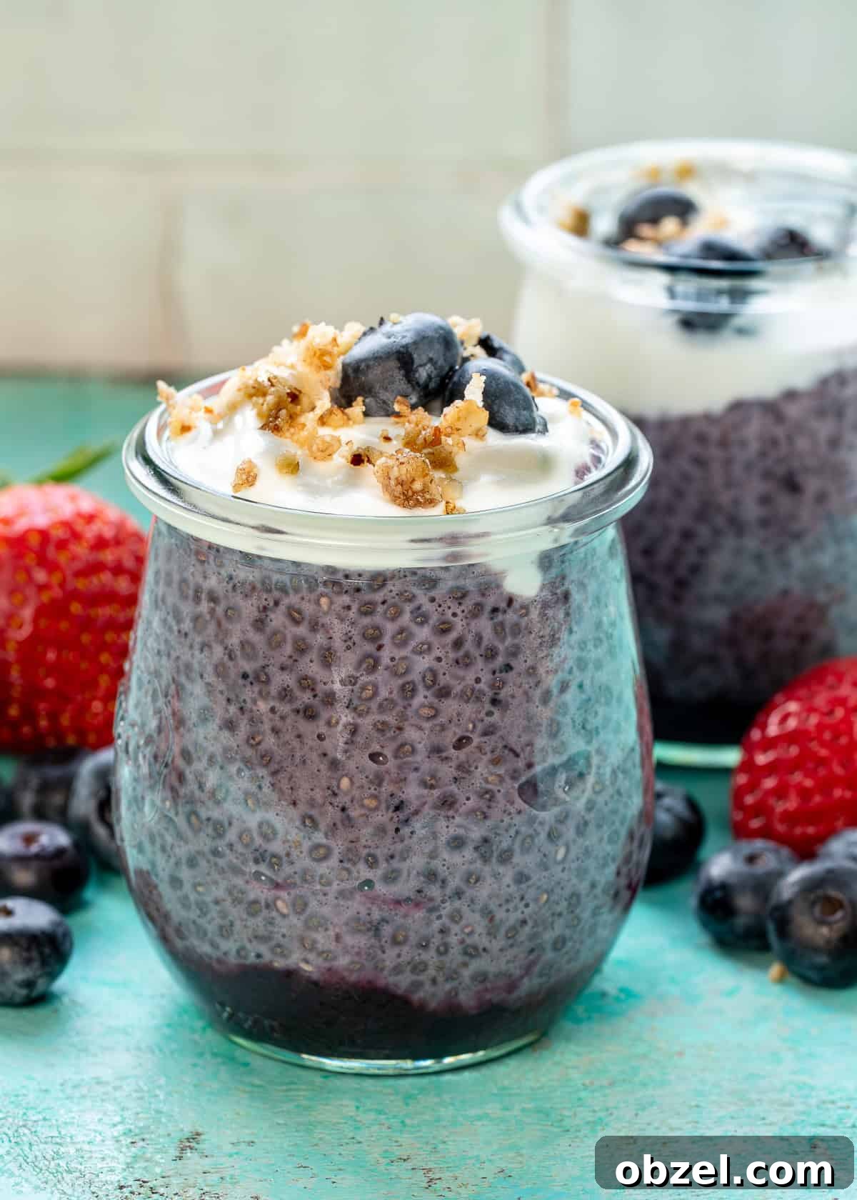 two jars of blueberry chia pudding on a counter surrounded with fruit