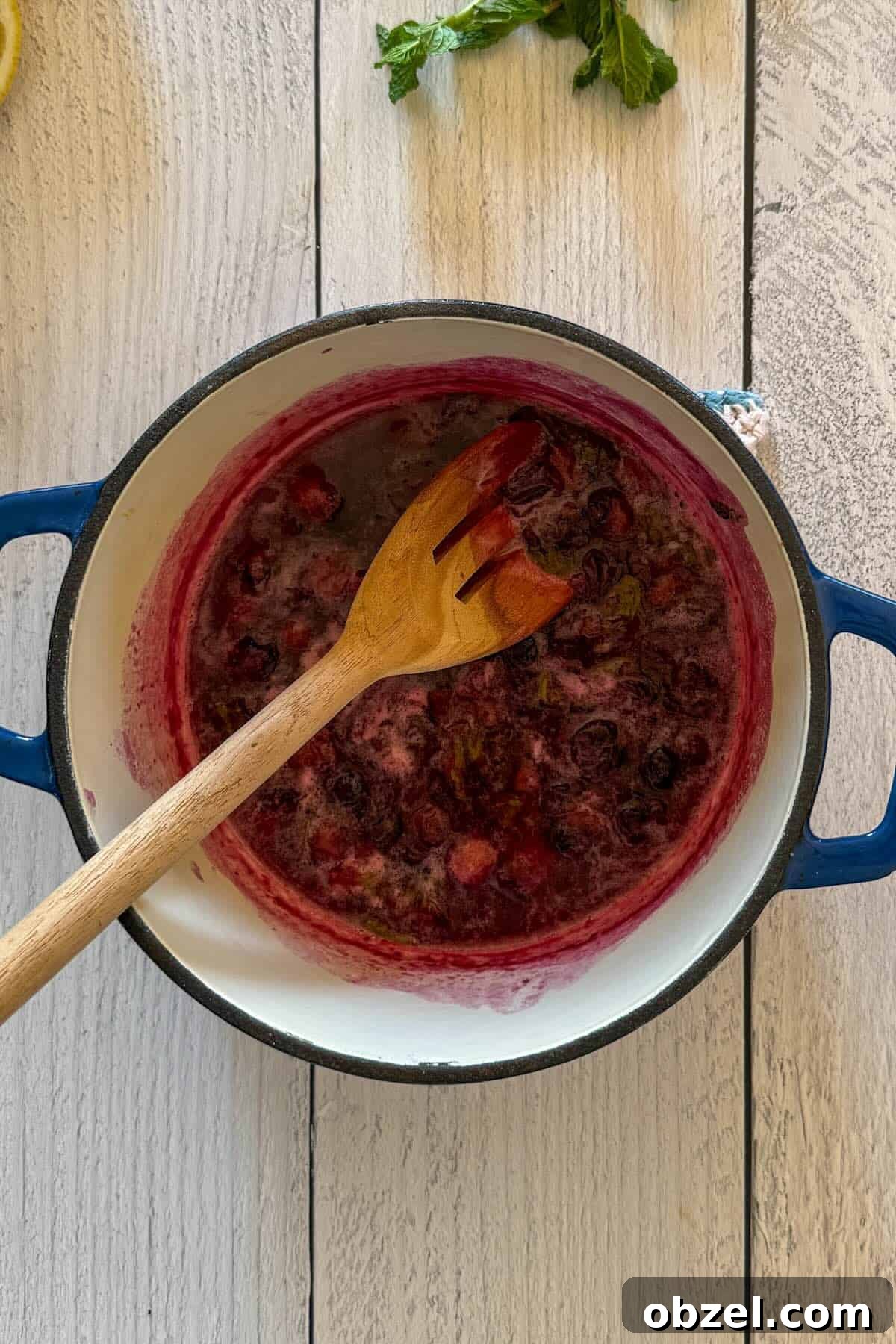 Crushing the blueberries with a wooden spoon to release their juices.