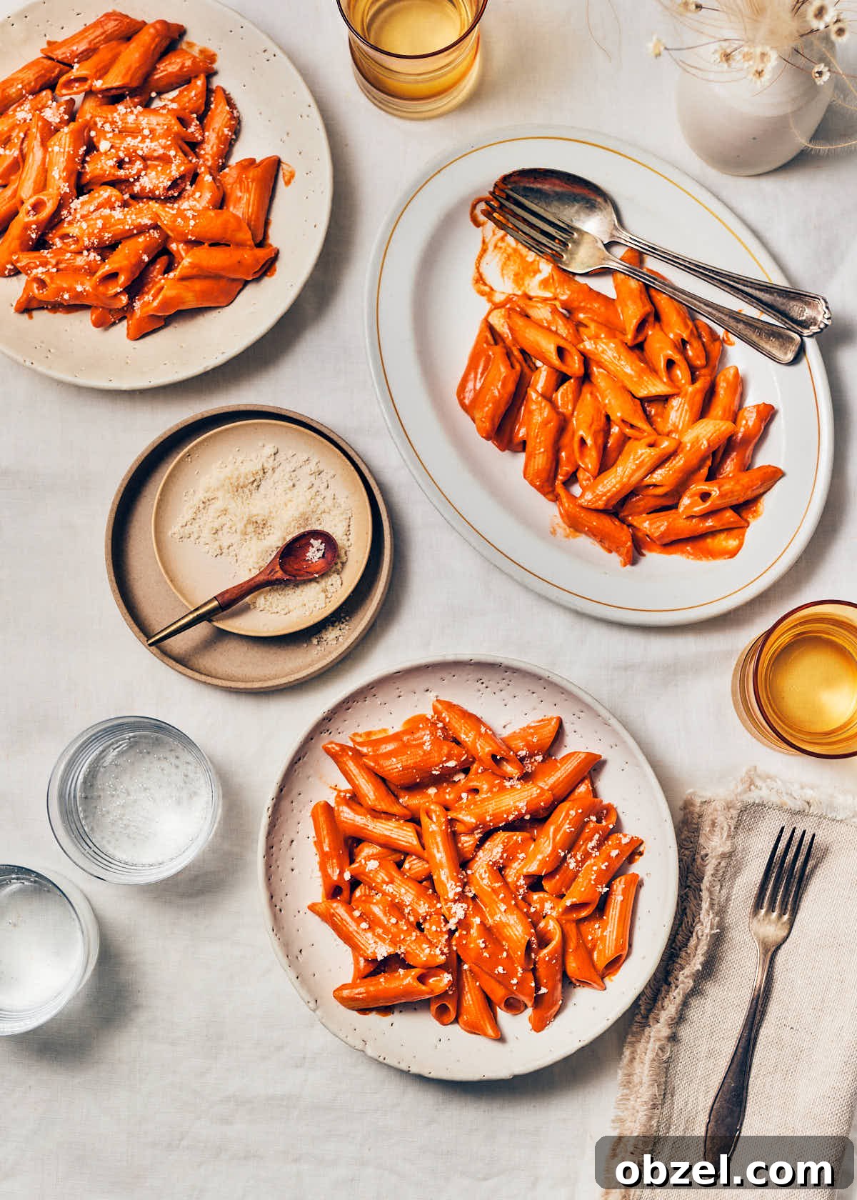 Creamy Vegan Vodka Sauce Pasta 15 A dinner table with plates of vegan vodka sauce pasta, water glasses, small dish of vegan parmesan cheese