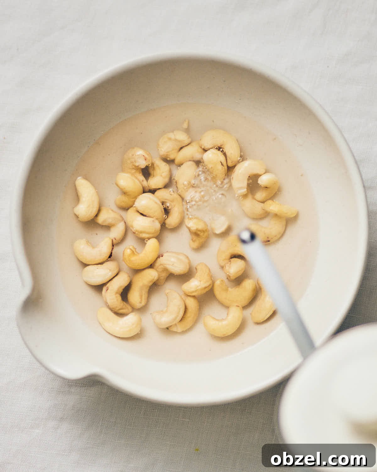 Creamy Vegan Vodka Sauce Pasta 8 A white bowl of raw cashews with hot water from a kettle being poured on top.