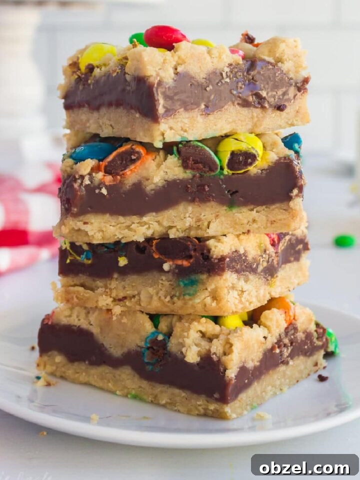 Close up of a stack of M&M Chocolate oat bars with a glass of milk in the background.